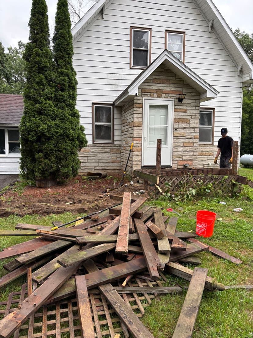 Home renovation project with stacked wooden planks and worker beside a house under construction.