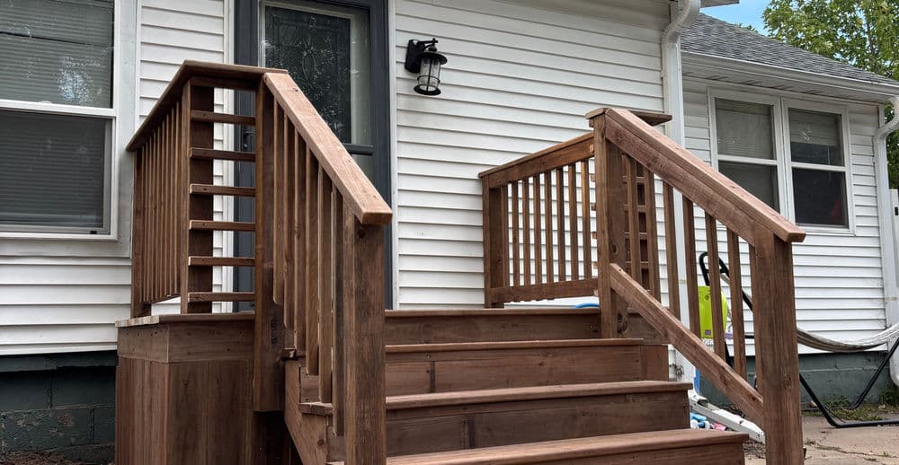 Wooden stairs with railings leading to a white house exterior, featuring a porch light.