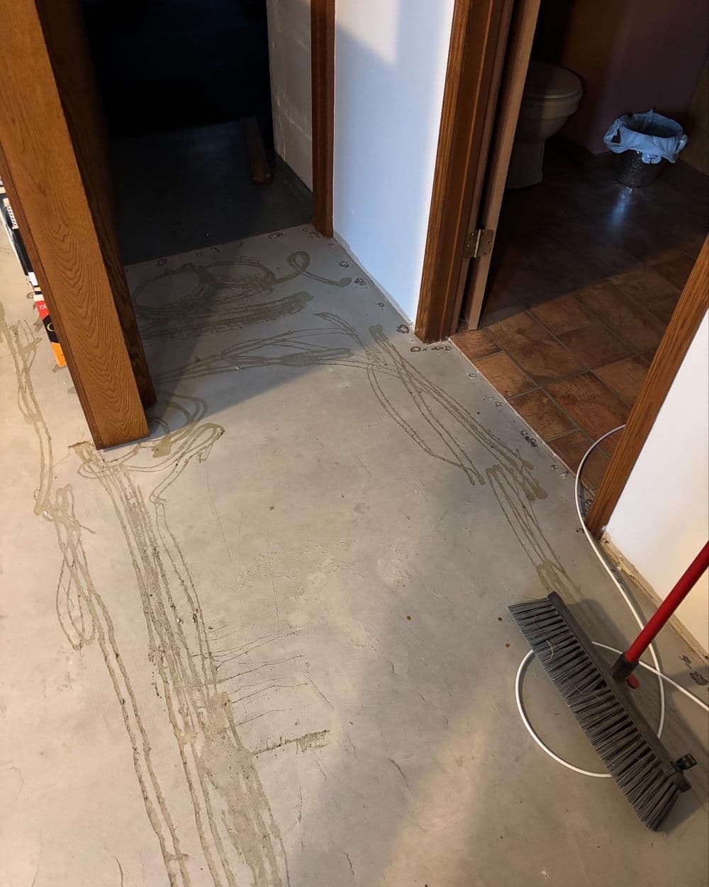 Skeleton outline on concrete floor in a hallway, with broom and bathroom visible.
