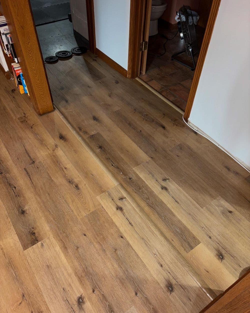 Wooden flooring transition between rooms in a home, showcasing textured planks and doorways.