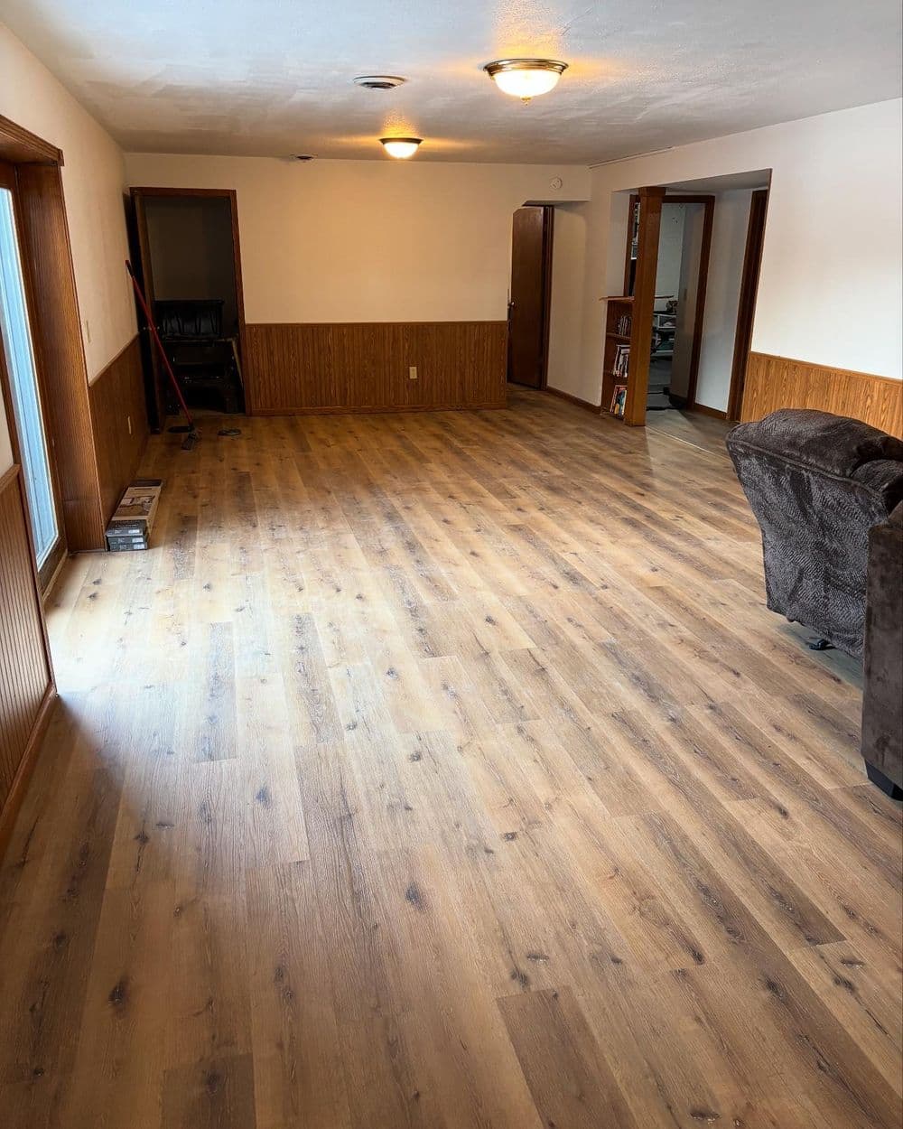 Spacious living room with wood flooring, natural light, and wooden paneling accents.
