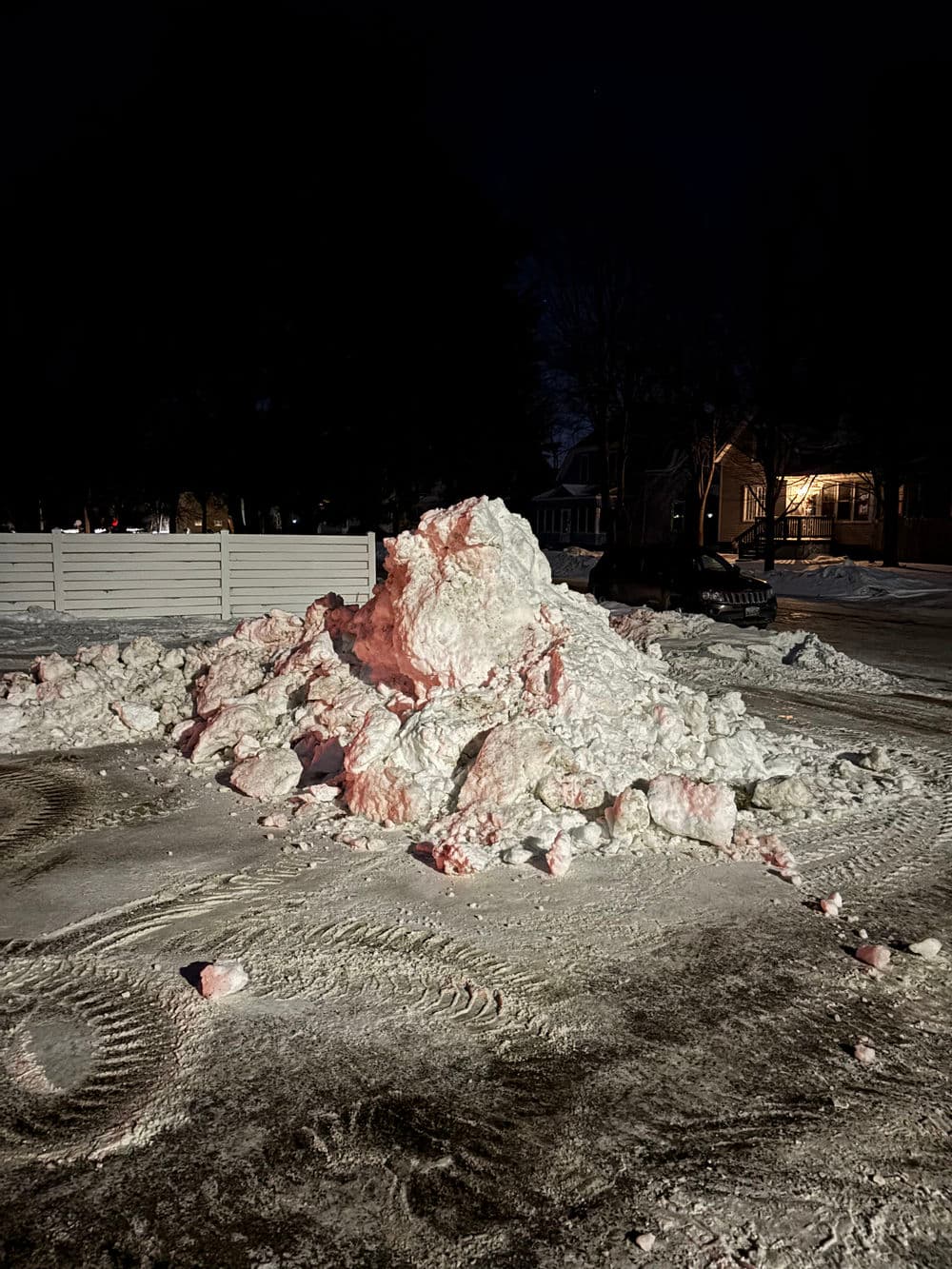 Snow pile in a parking lot at night, illuminated by nearby lights.