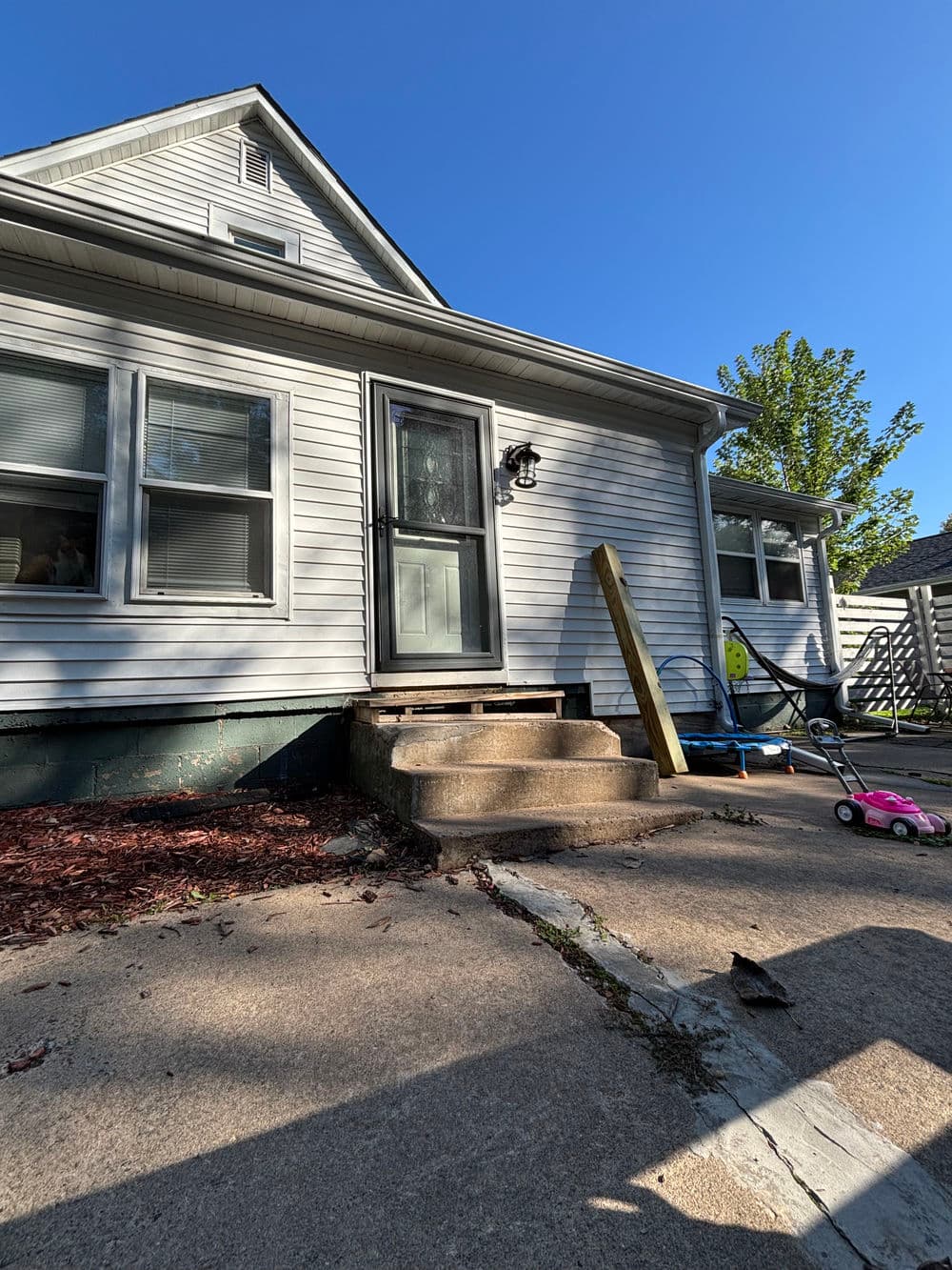 Front entrance of a house with steps, sunlight, and a pink toy car nearby.