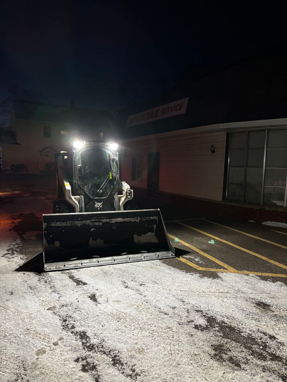 Snow plow at night clearing parking lot in front of tax service office.