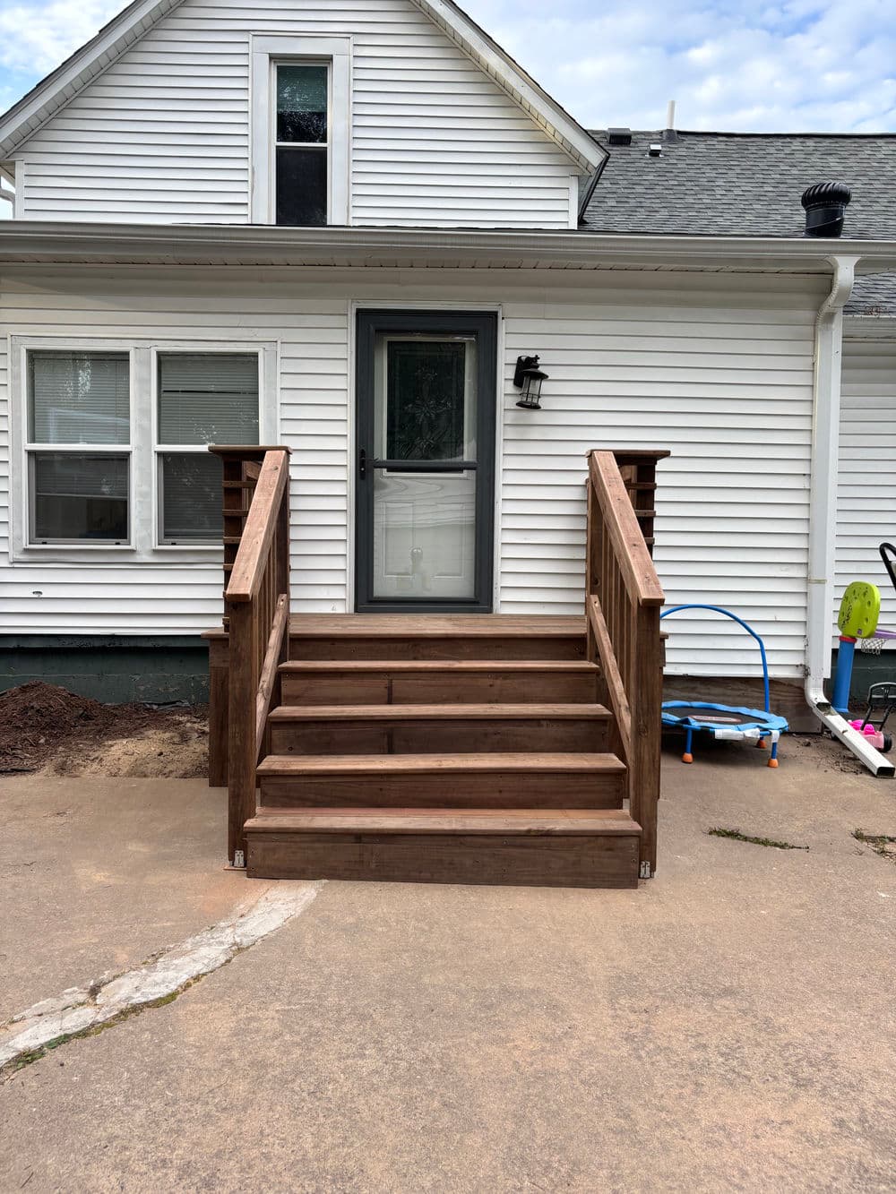 Newly built wooden front steps leading to a house with a gray door and surrounding yard.