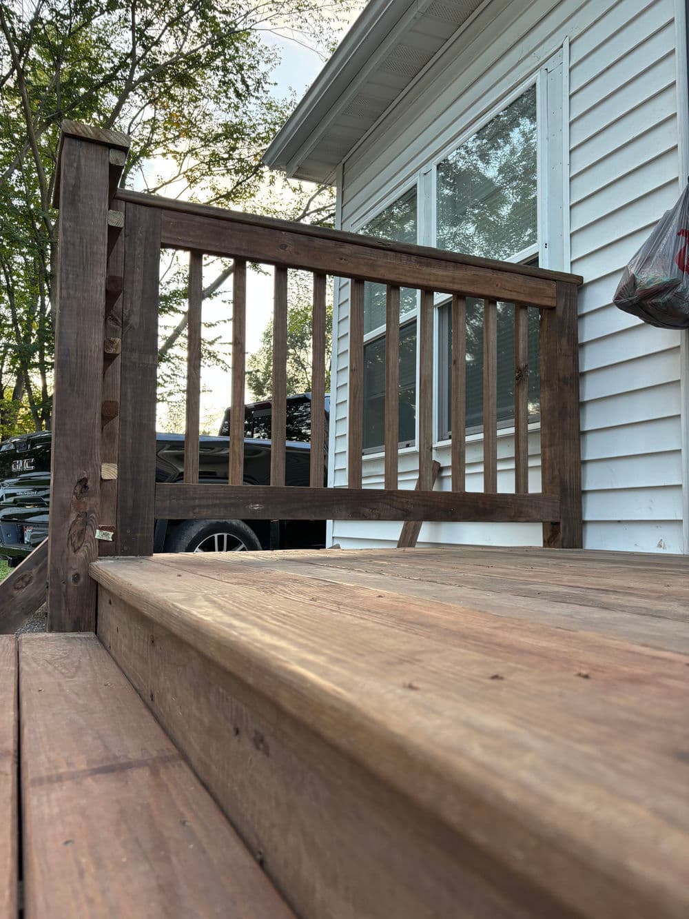 Wooden porch railing and steps leading to a house, surrounded by greenery.