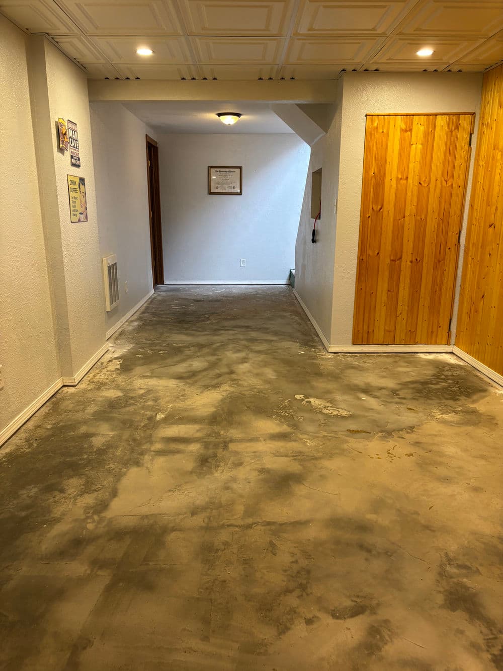 Interior hallway with unfinished concrete floor, light walls, and wooden door. Brightly lit space.