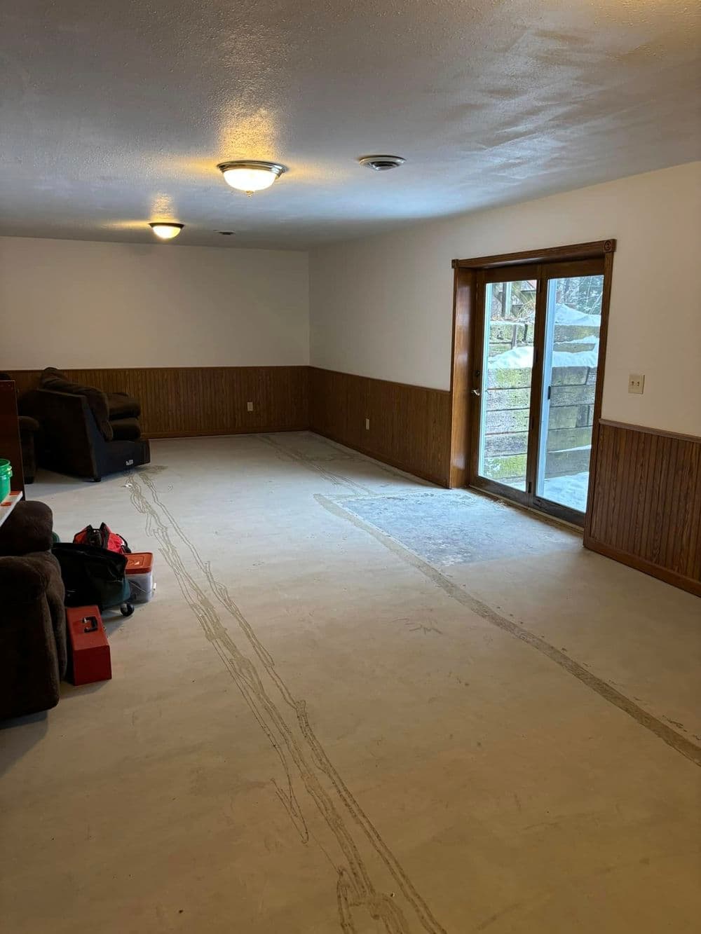 Empty room with concrete floor, wooden paneling, and sliding glass door to outdoor area.