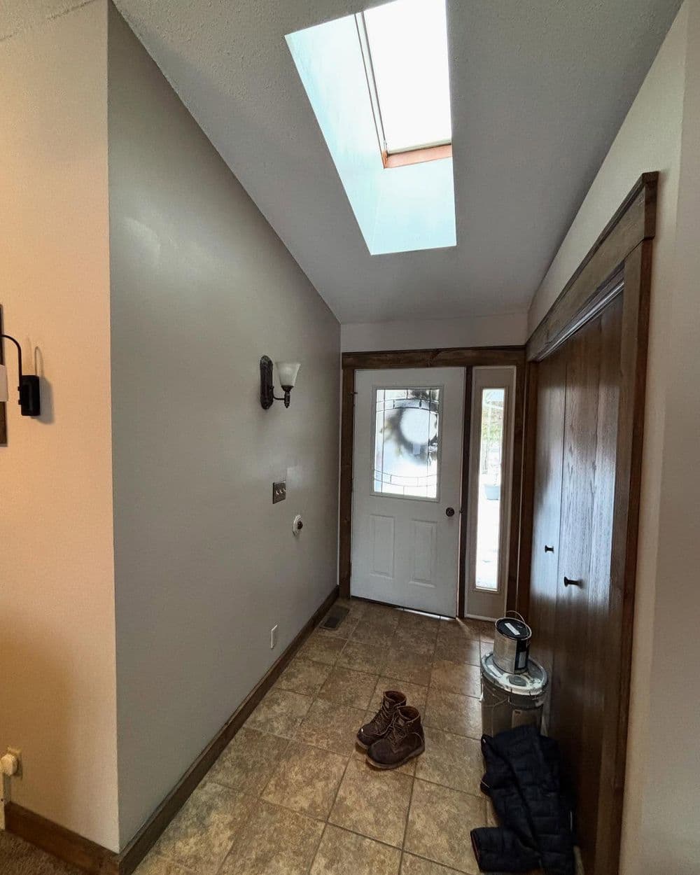 Bright foyer with skylight, wooden trim, and tiled floor, featuring a front door and shoes.