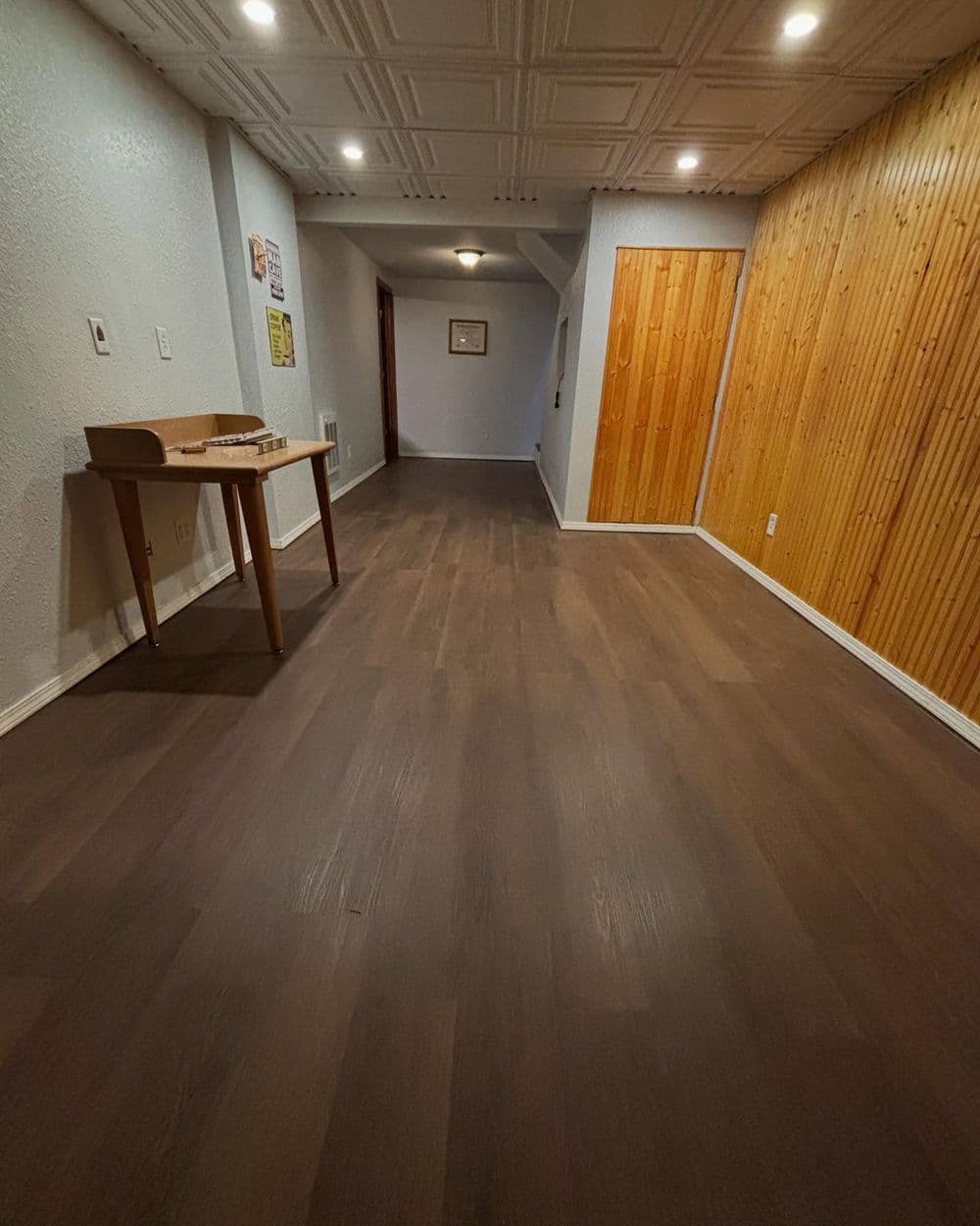 Spacious hallway with wooden flooring, wall paneling, and modern lighting fixtures.