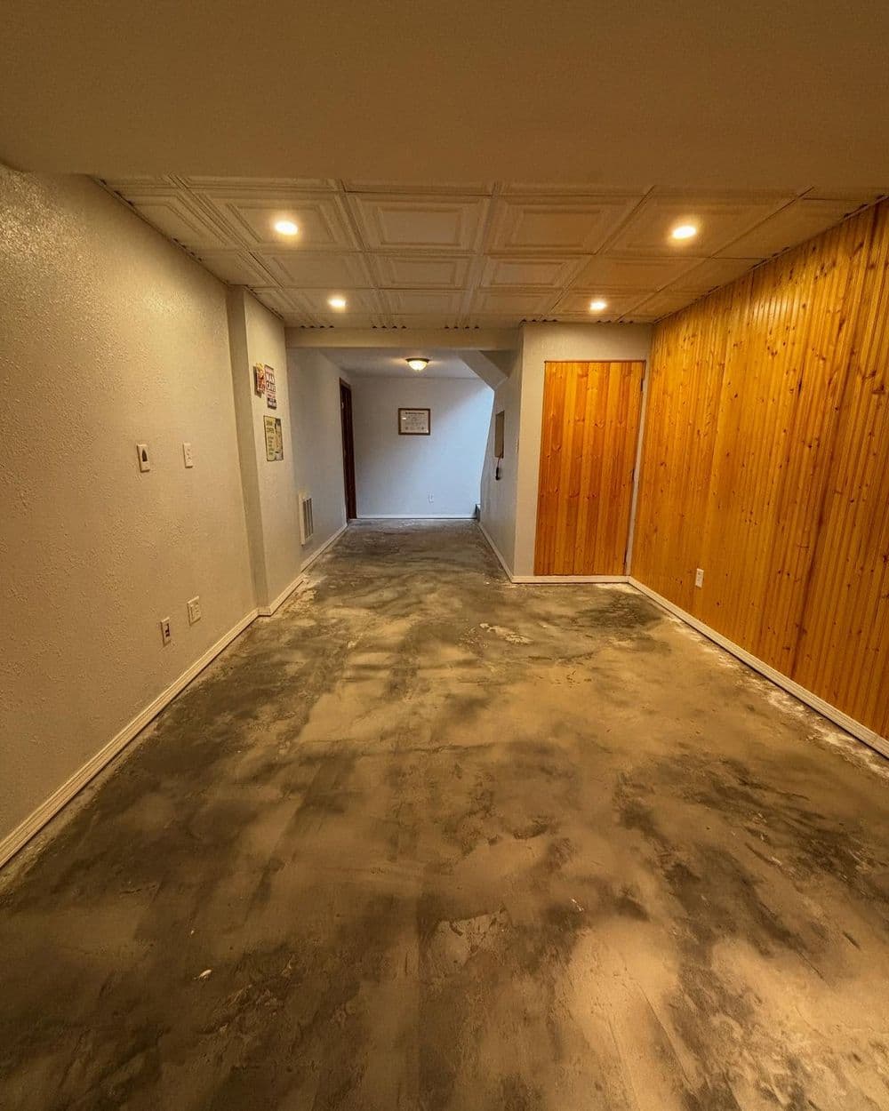 Narrow hallway with textured walls, wooden paneling, and unfinished concrete flooring.