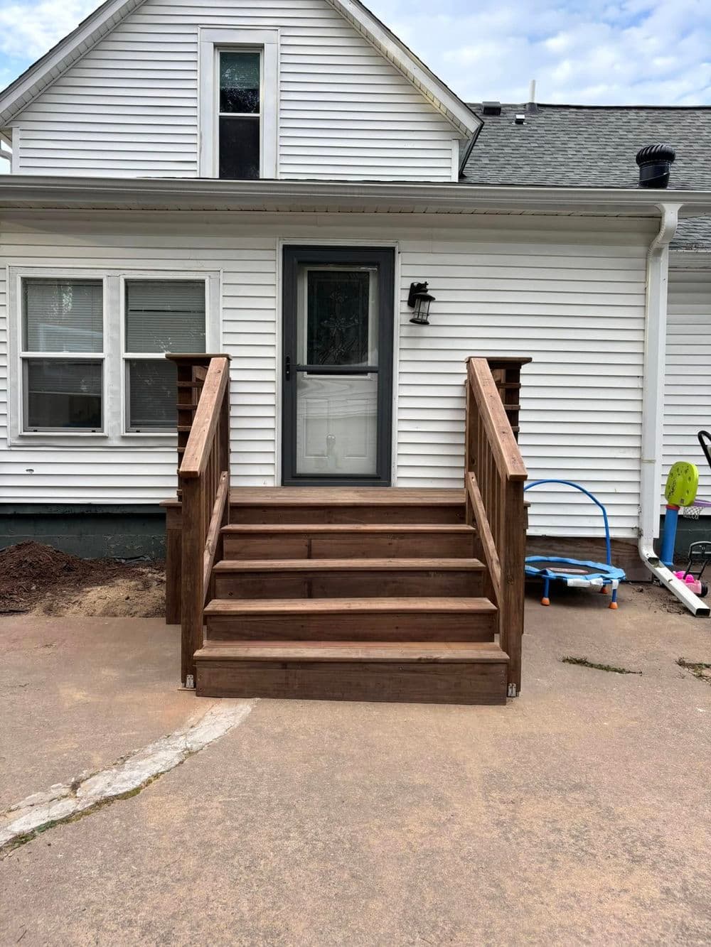 Wooden steps leading up to a white house with a grey door and porch.