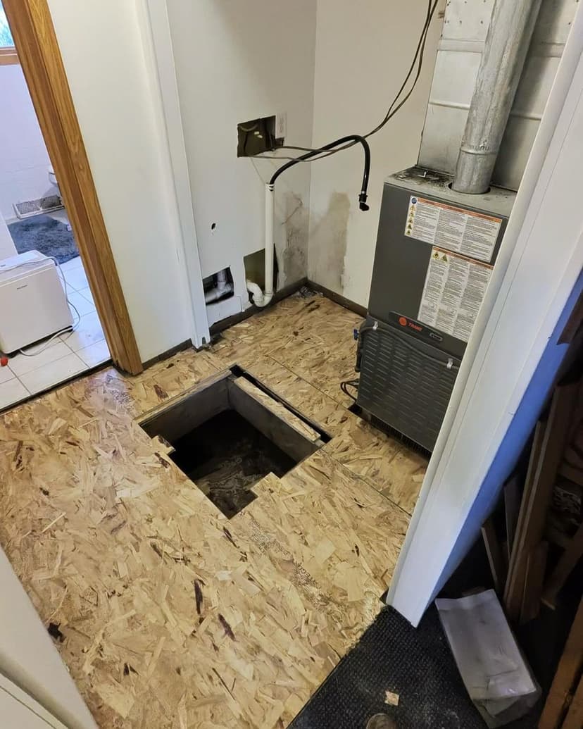 View of a room with exposed floor and HVAC unit, showing a cutout in the plywood flooring.