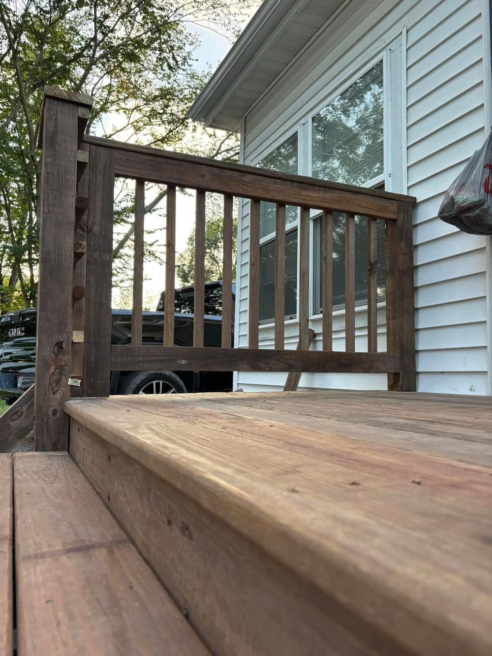 Wooden porch railing and steps leading to a white house, surrounded by greenery.