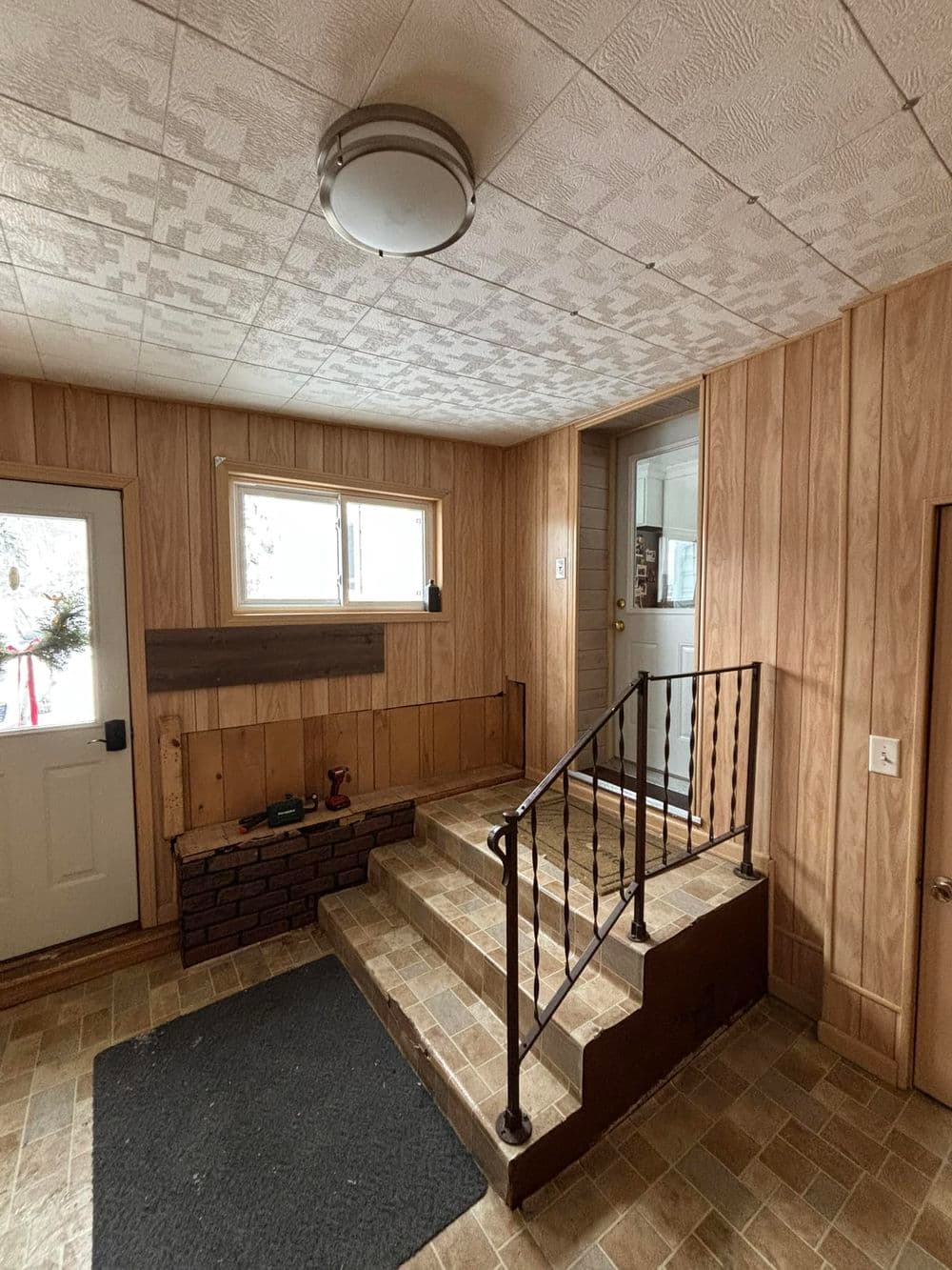 Interior entryway with wooden paneling, staircase, and welcoming light fixture.