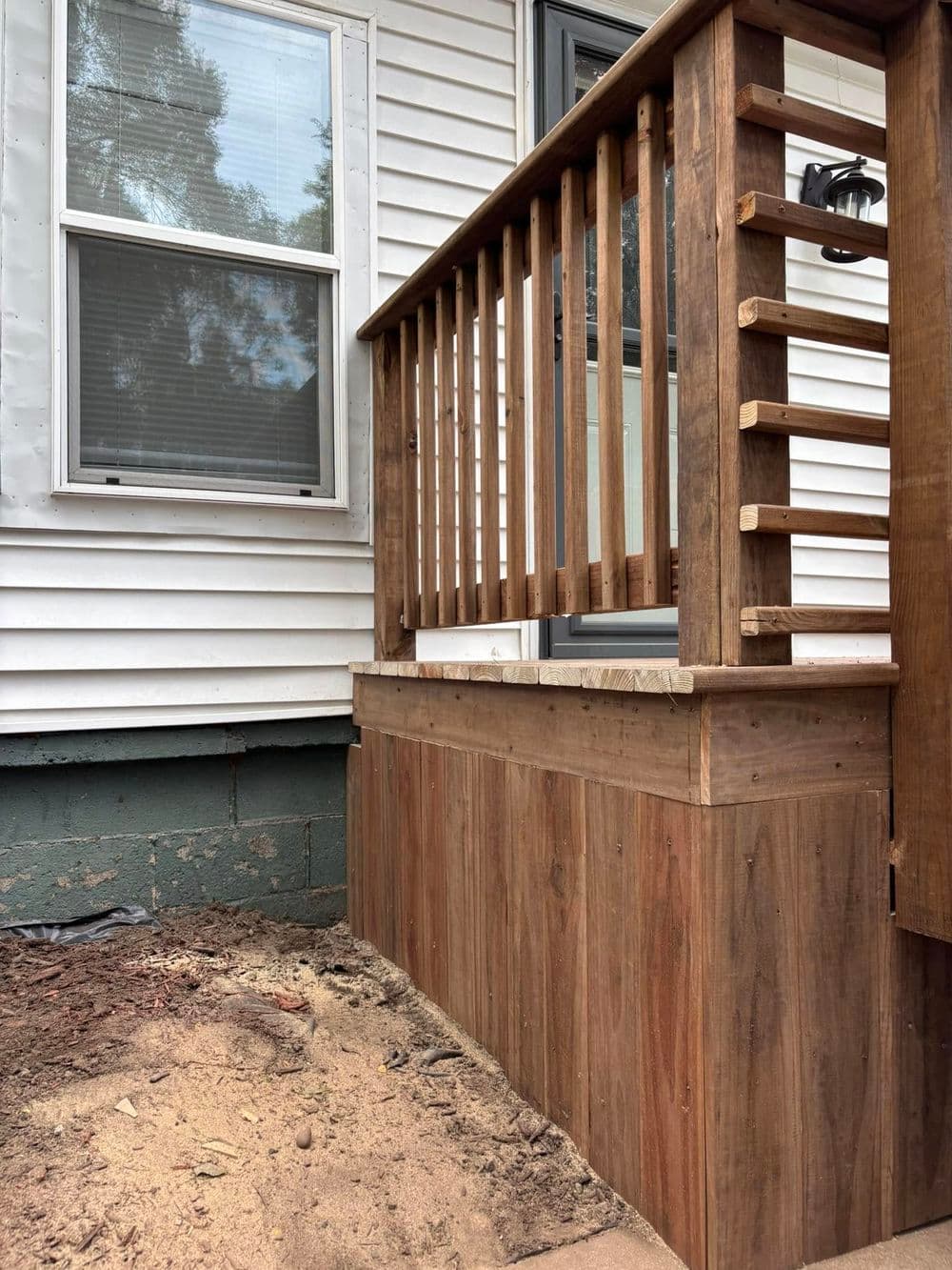 Wooden railing on a porch with a freshly built base against a house exterior.