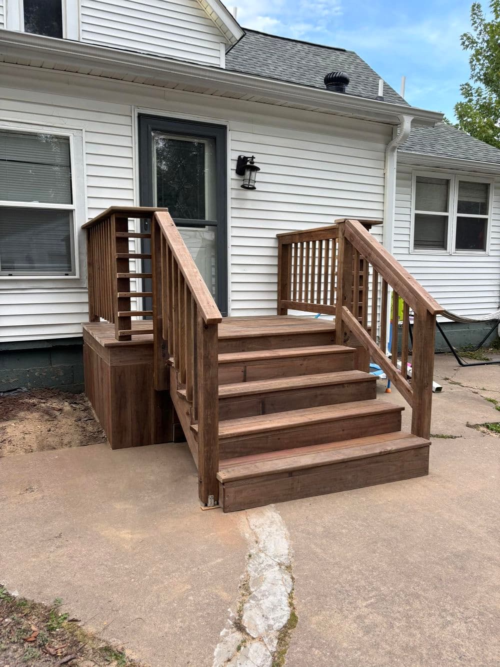 New wooden steps and railing leading to a white house entrance with a porch.