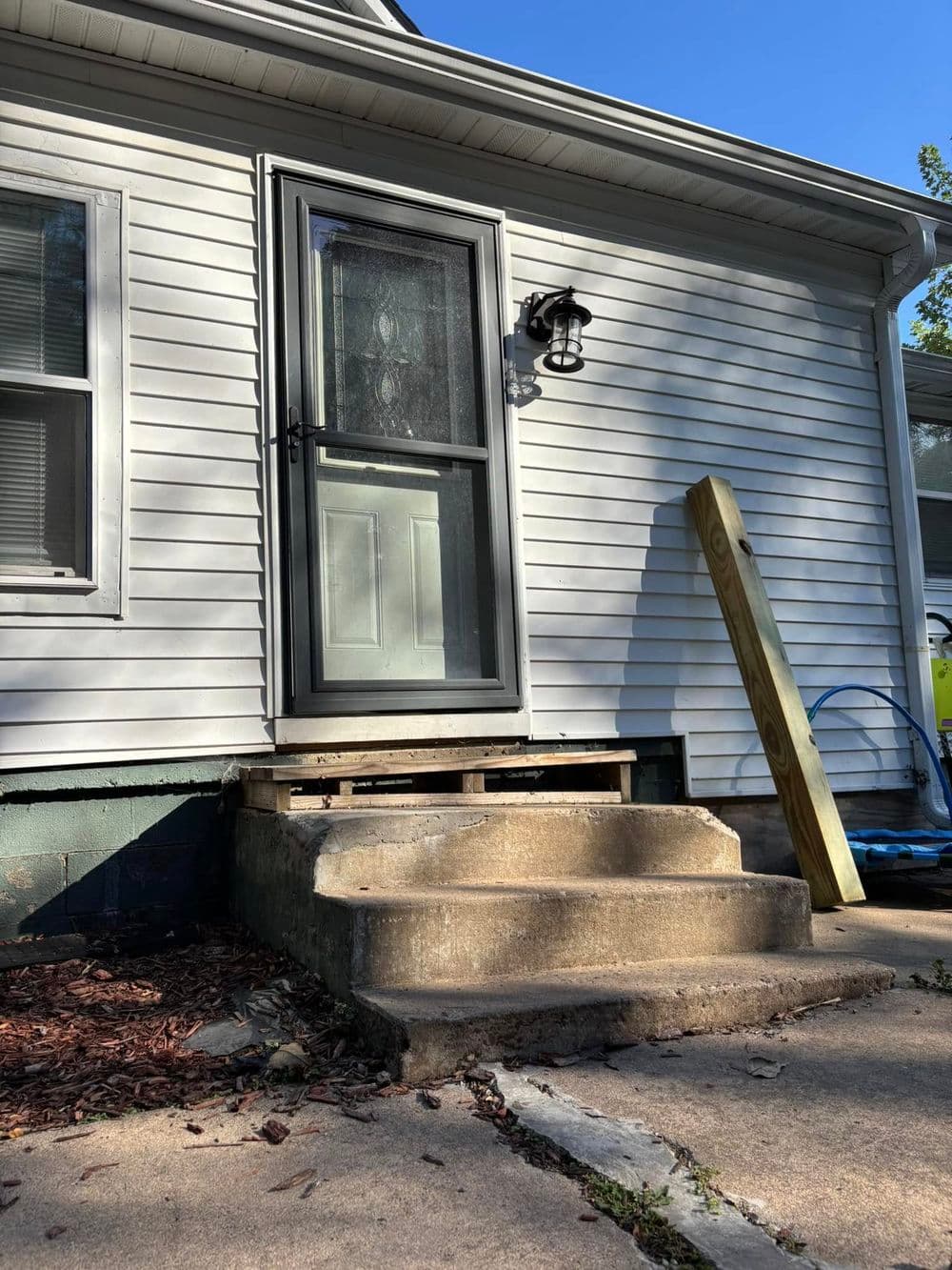 Front entrance of a house featuring a wooden ramp and concrete steps in natural light.